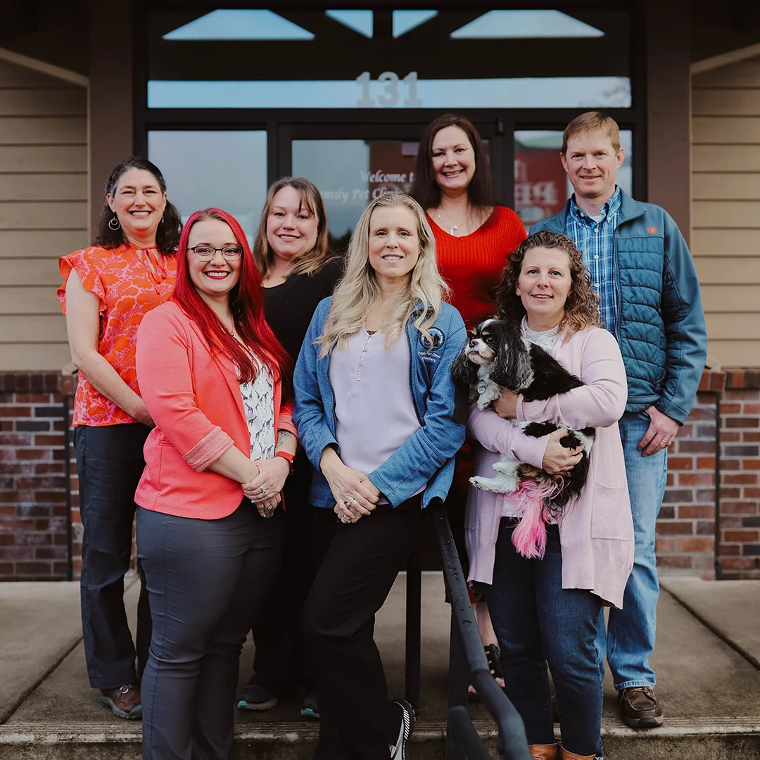 Group of seven smiling veterinary staff members posing outside the clinic entrance, with one person holding a small dog.